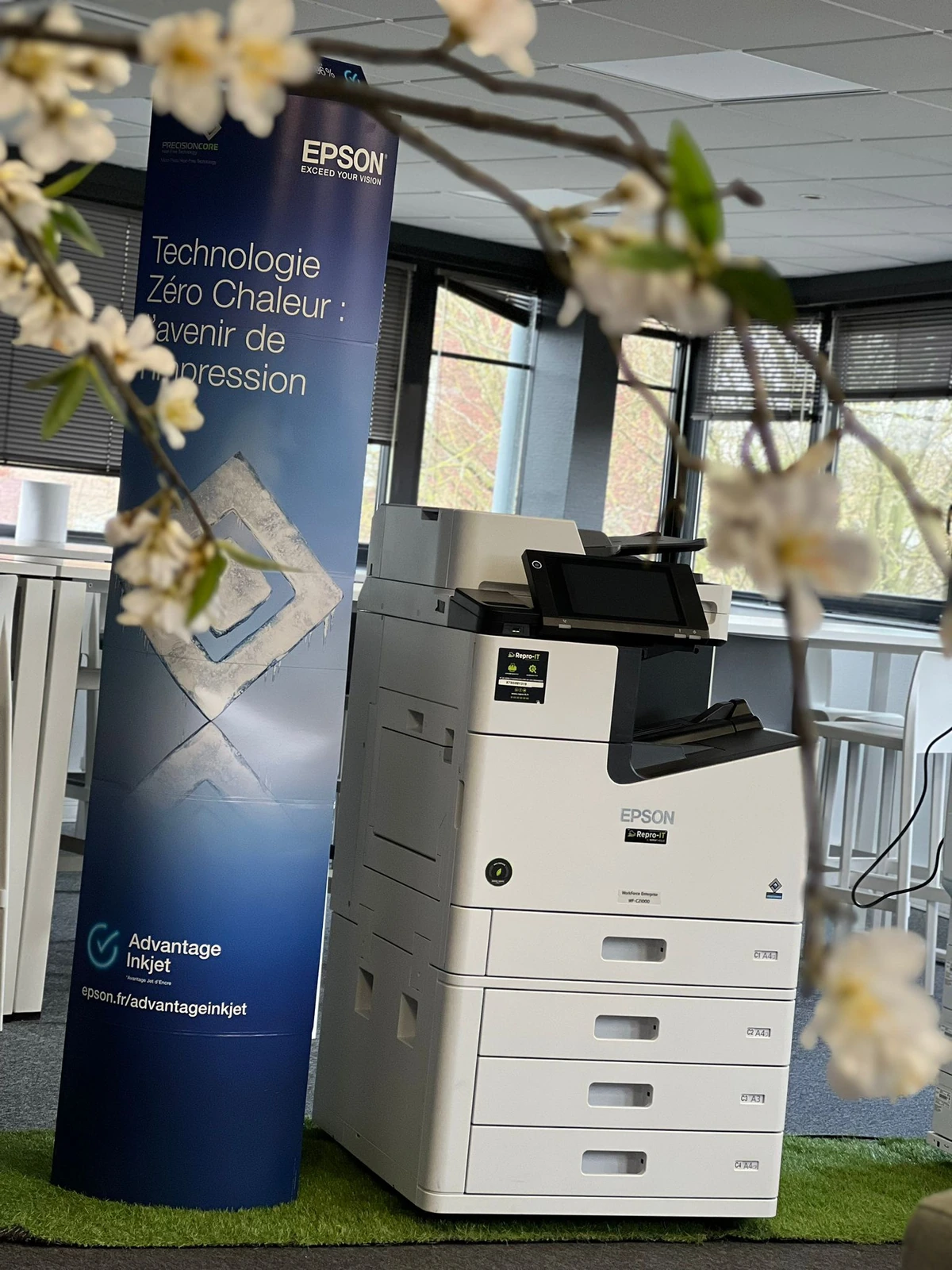 Photocopieur Epson dans l’espace de présentation Repro-IT, derrière des branches fleuries